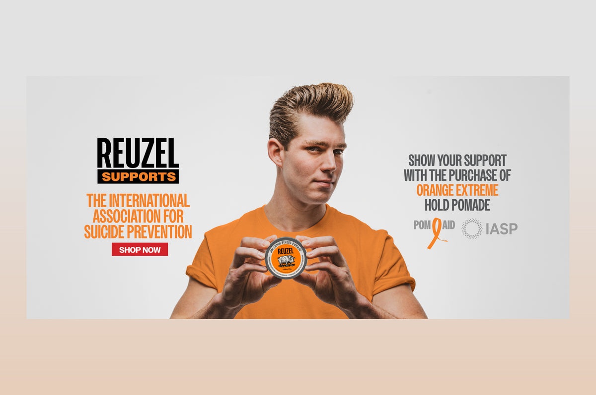 A promotional graphic for Reuzel Supports featuring a man in an orange T-shirt holding a tin of orange pomade. Text on the left reads 'REUZEL SUPPORTS' with 'THE INTERNATIONAL ASSOCIATION FOR SUICIDE PREVENTION' and a 'SHOP NOW' button.